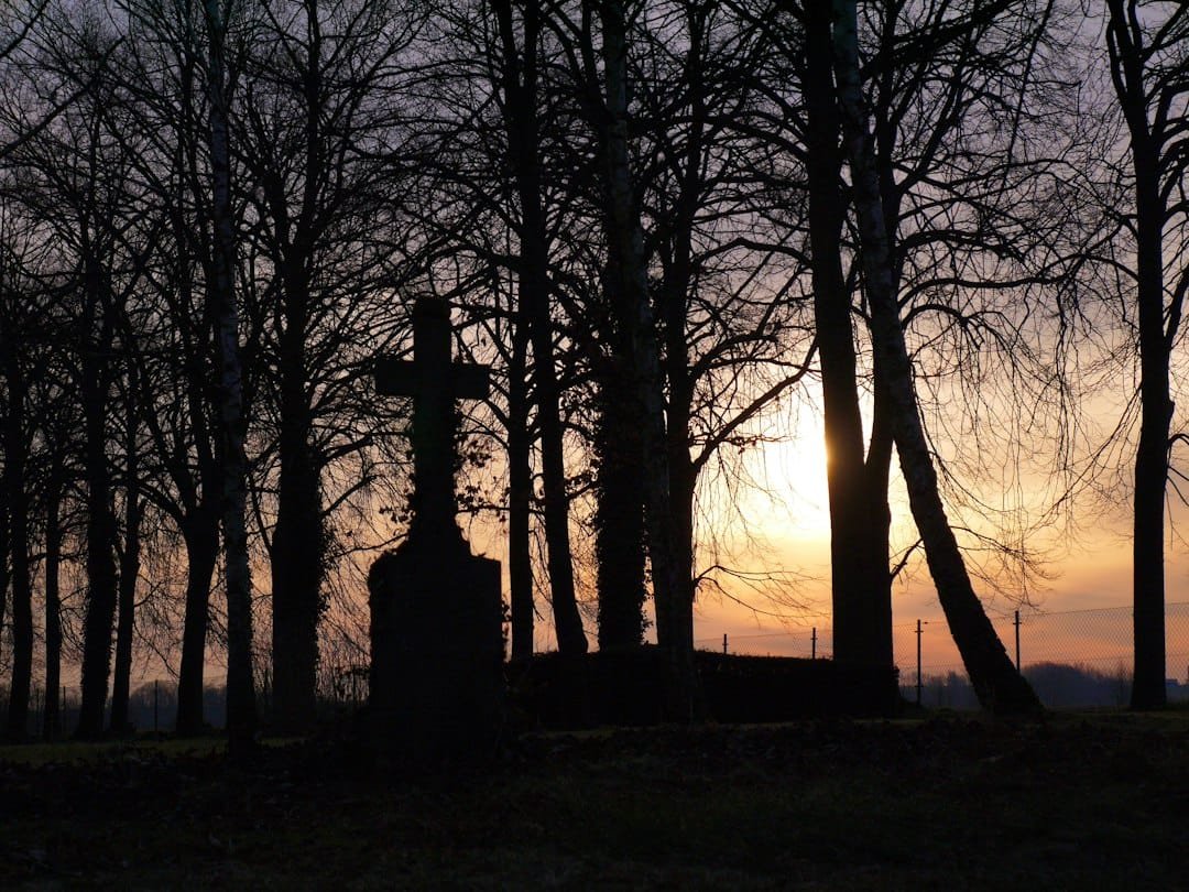 cruz de cementerio recortada contra un atardecer, símbolo de la oración por los difuntos