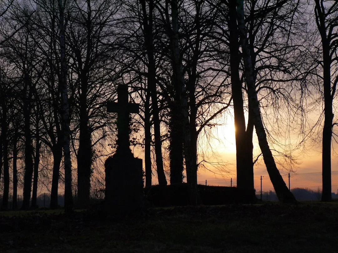 cruz de cementerio recortada contra un atardecer, símbolo de la oración por los difuntos